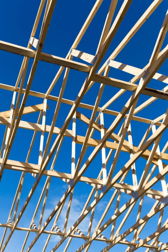 Charpente bois construction : structure de toit et ciel bleu. Charpente en bois d'un toit en construction, vue de dessous, révélant la structure des fermes contre un ciel bleu intense et lumineux.